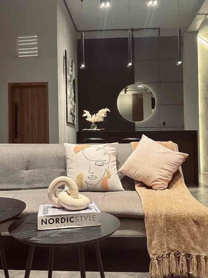 Gray and brown toned living room featuring a sofa and coffee tables at center, with round mirror and wall decor adding natural modern style