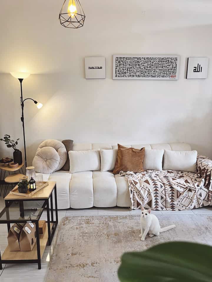 White and brown toned living room featuring cream sofa, patterned carpet, floor lamp and side tables with a calming, simple natural atmosphere