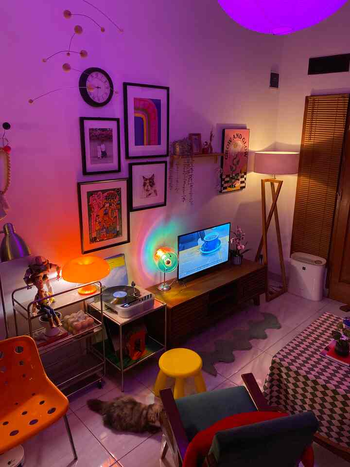 Mid-Century Modern living room with purple lighting, featuring a yellow stool and orange chair, and a cat sitting on the floor in a cozy atmosphere