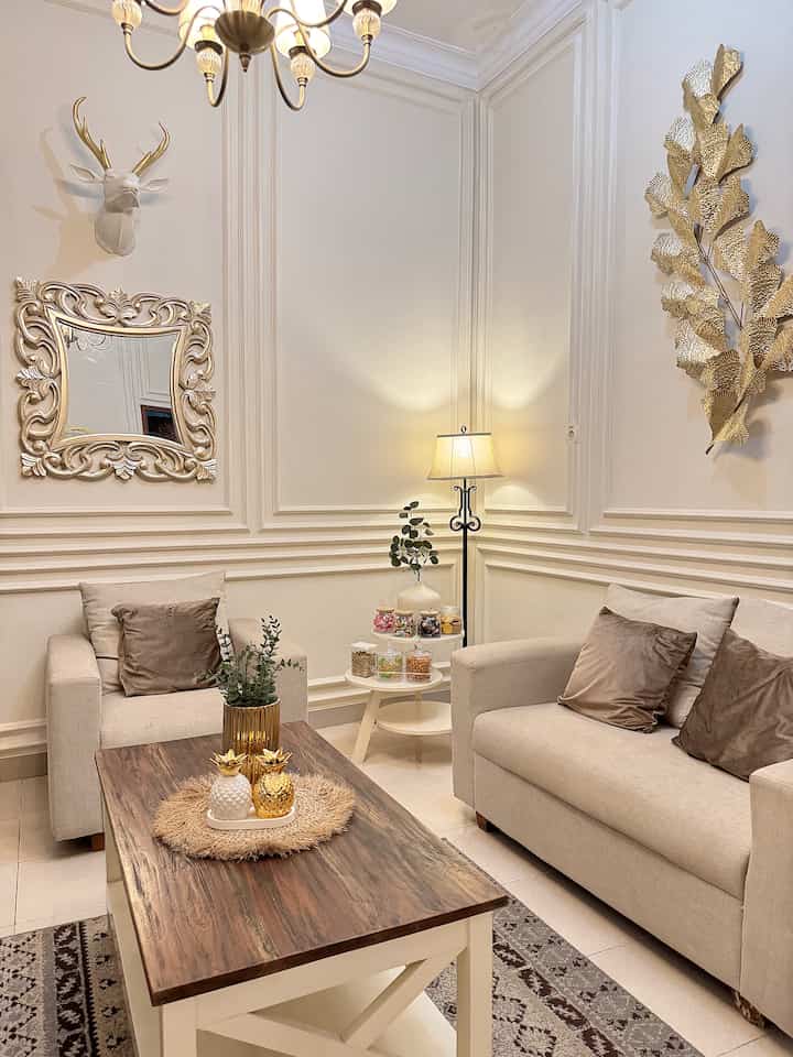 Beige-toned living room featuring two beige sofas, brown coffee table, gold wall decor, and cozy lighting