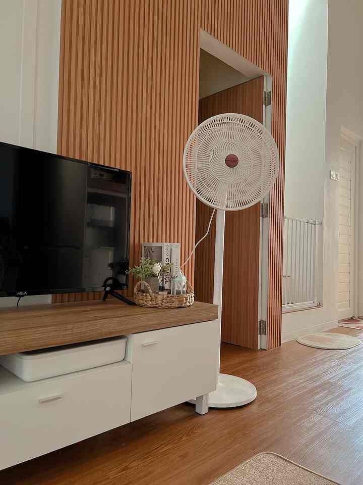 Natural wood-toned living room featuring a TV stand, shelf, and white standing fan in a cozy setting