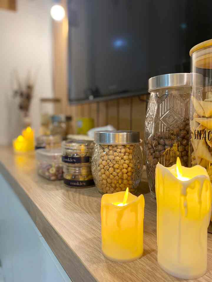Warm yellow-lit kitchen space featuring transparent glass jars and candles arranged on a wooden table