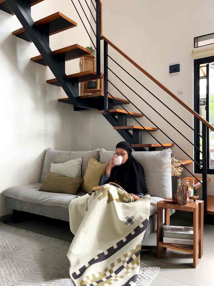 Natural toned living room featuring a gray sofa and wooden stairs, creating a cozy space for reading and enjoying coffee