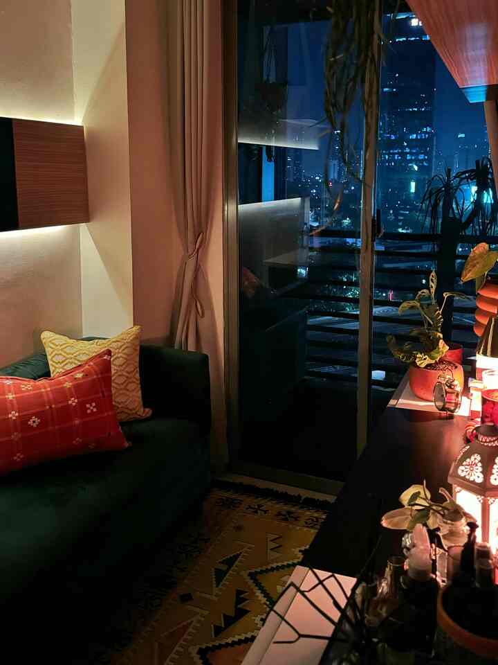 Warm yellow-toned bohemian apartment living room featuring cozy cushions and a night city view through the sliding window