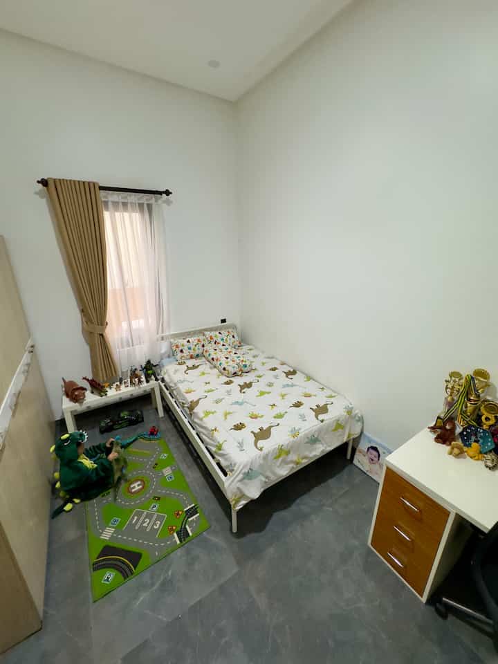 Bright kids' room with white walls and minimal furniture, featuring dinosaur-patterned bedding and a play mat for a cozy vibe