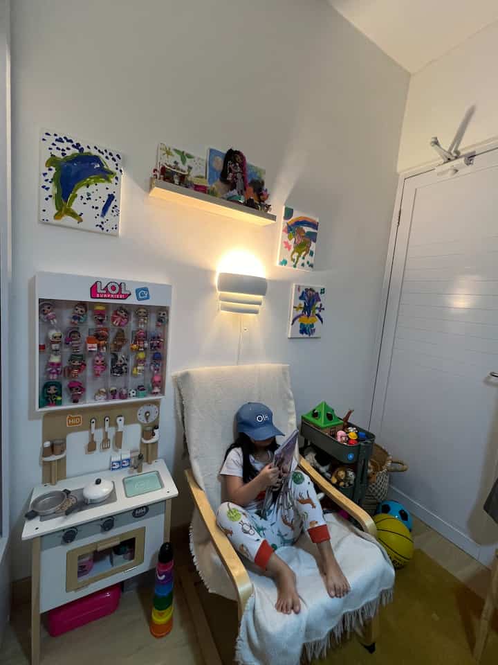 Bright white and natural wood toned kids' room featuring an armchair, toys, and children's artwork creating a cozy atmosphere