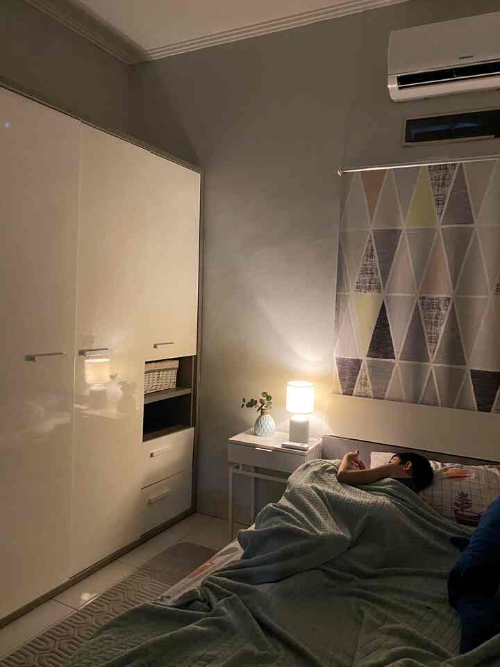 A cozy kids' room with gray walls and white furniture, featuring pastel bedding and a nightstand lamp illuminating a sleeping child