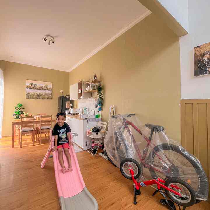 Beige-walled kitchen and dining area with wood-tone flooring, featuring a child on a pink slide in a cozy family space