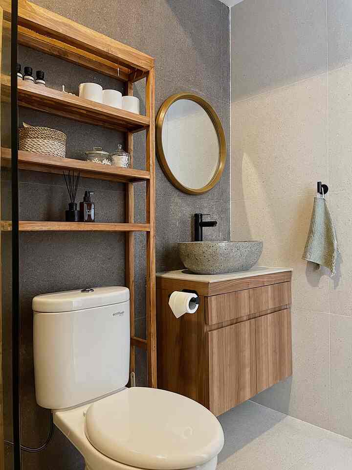 Natural-toned bathroom featuring wooden shelving and vanity with round mirror, sink, and toilet in a clean arrangement
