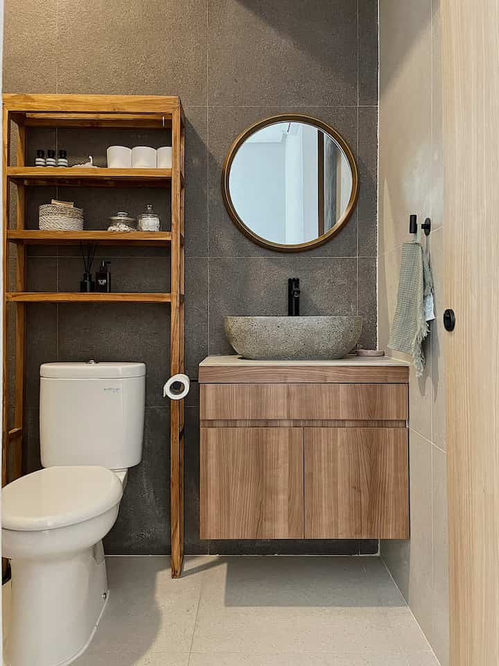 Natural and gray toned bathroom featuring wooden shelving, stone vessel sink, and round mirror creating a clean aesthetic