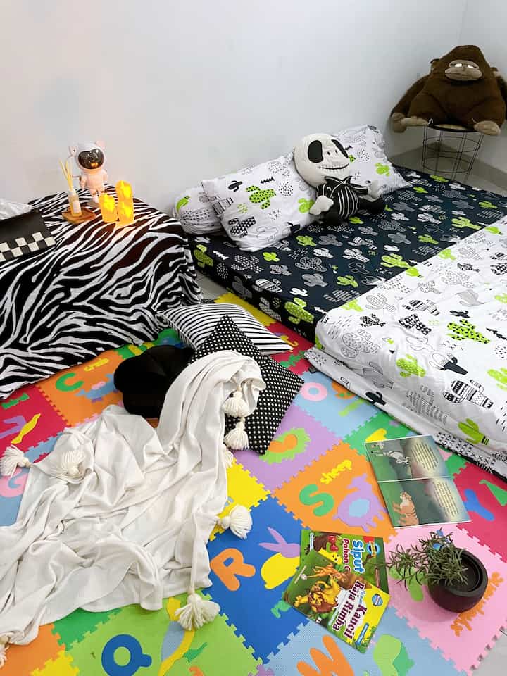 Monotone kids' room featuring cactus-themed bedding and colorful puzzle mat, with simple functional furniture layout