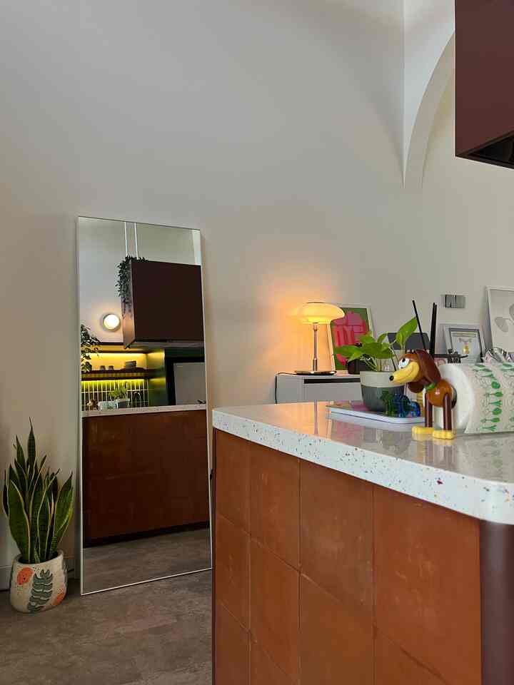 Natural color toned kitchen space with large full-length mirror, table lamp, and plants arranged creating a cozy atmosphere