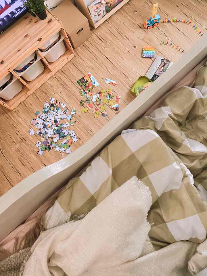 Wood tone floored bedroom featuring scattered toys, checkered bedding and a soft blanket creating a cozy atmosphere