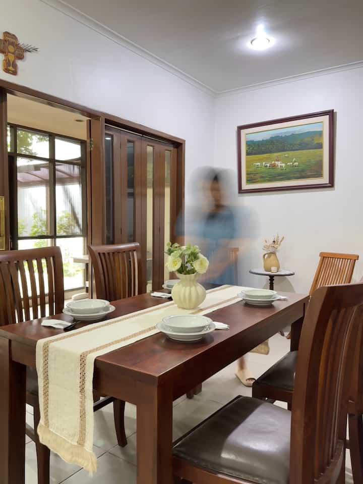 Simple dining room featuring brown wood furniture and white walls, with a table runner and a vase centrally placed on the dining table