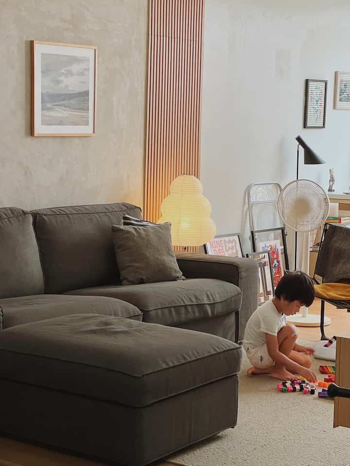 Natural toned living room featuring a gray sofa, warm lighting, and a child playing on the floor creating a cozy atmosphere