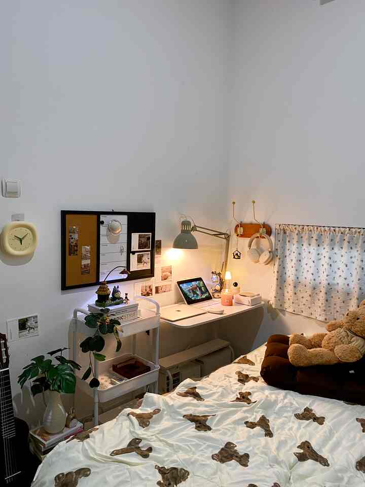 White and brown toned bedroom featuring bear-pattern bedding, cushions, a workspace desk and lamp creating a cozy atmosphere