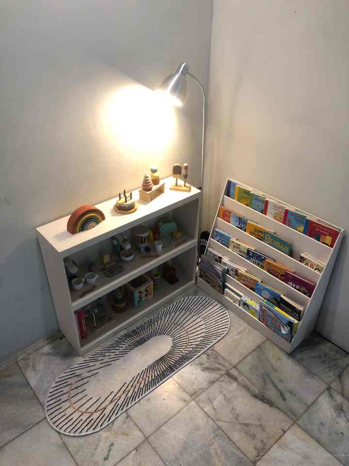 Corner kids' room with white walls and furniture, featuring children's toys and bookshelf, illuminated by a floor lamp creating cozy atmosphere