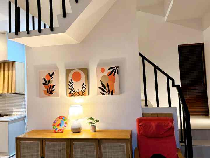 White-walled space with wooden storage cabinet, red armchair, modern wall art, and a lamp creating a cozy atmosphere