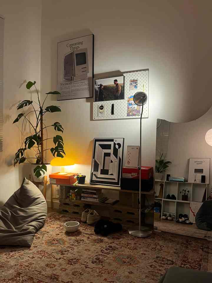 A cozy bedroom with warm natural tones featuring a bean bag, floor lamp, plants, and wall art under ambient lighting