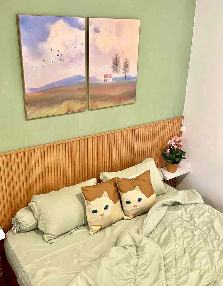 Soft green and beige toned bedroom featuring cat cushions and natural wood headboard creating a cozy atmosphere