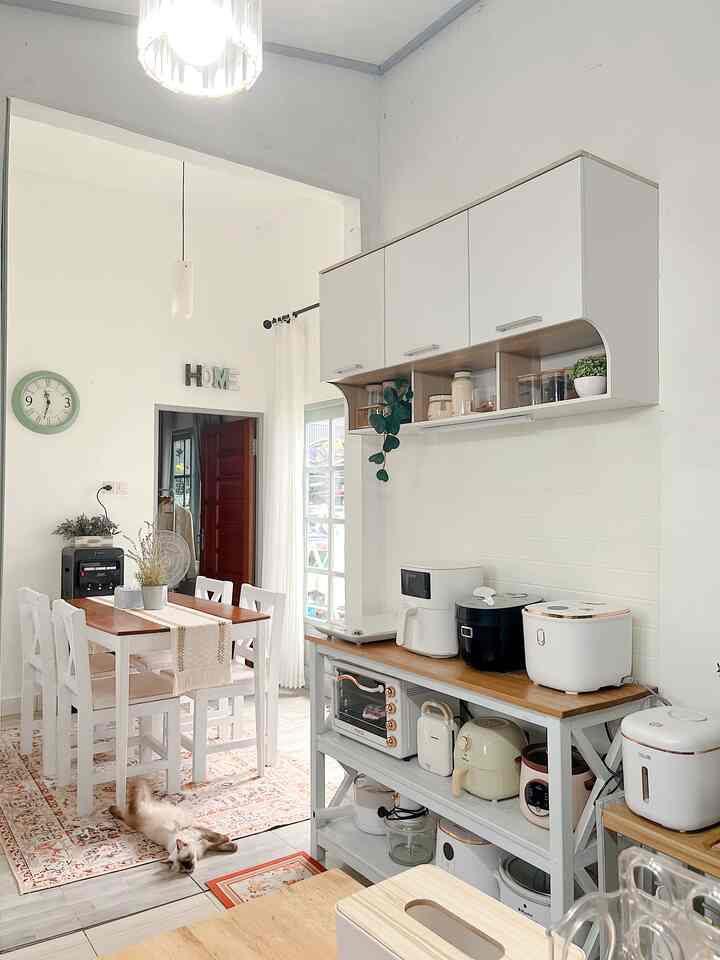 White and wood tone kitchen space featuring dining table, various kitchen appliances, and a relaxed cat lying on the rug in a cozy interior