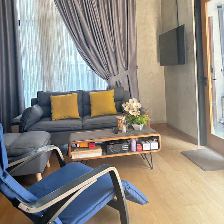 Gray-toned living room with natural wood floor, featuring gray sofa, blue armchair, and yellow cushions in a cozy setup