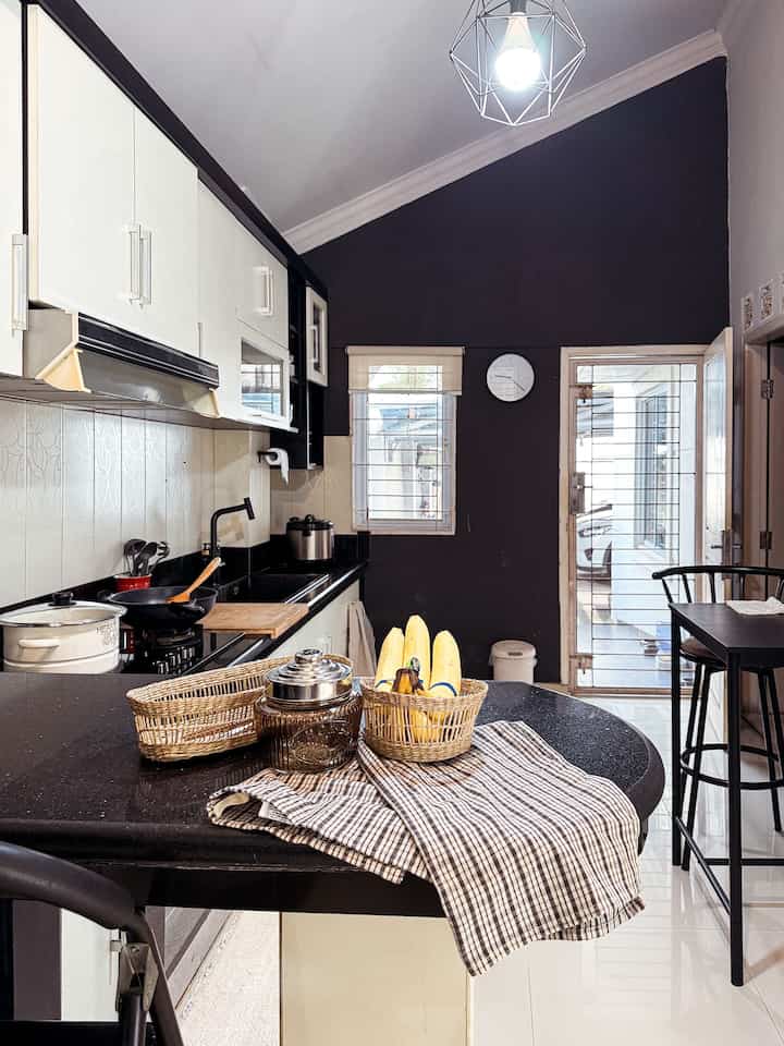 Black and white toned kitchen featuring bar stools, woven baskets on the island table, and clean modern lighting creating a neat atmosphere