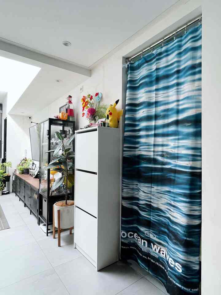 White walls and floors with black furniture and a blue ocean wave fabric poster, arranged in a narrow, tidy entrance space