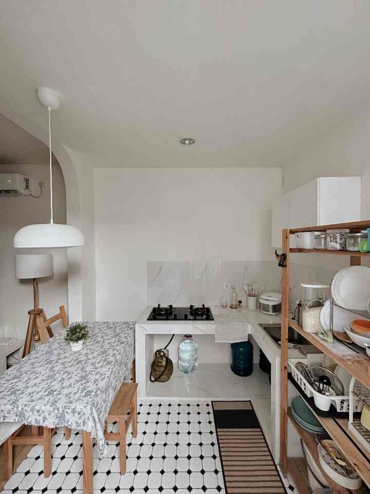 White walls and wood tone shelves in a minimal kitchen space, featuring a pendant light and tidy storage with a warm and cozy atmosphere