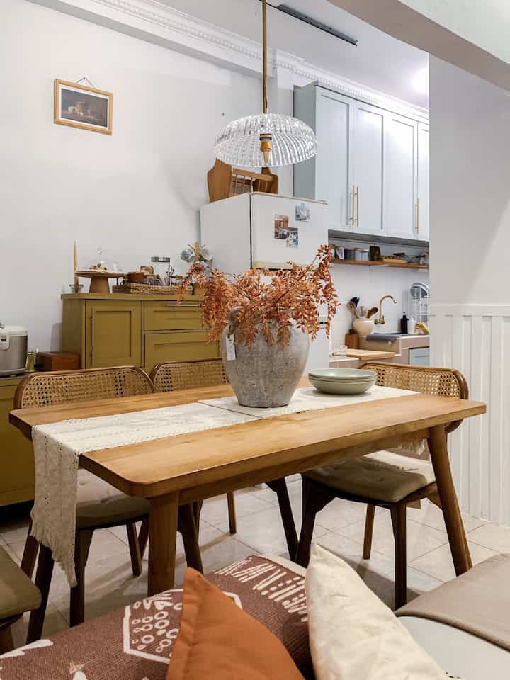 White-walled dining room with wood-tone furniture showcasing vintage style, featuring a table runner and dried flower centerpiece on the wooden dining table.