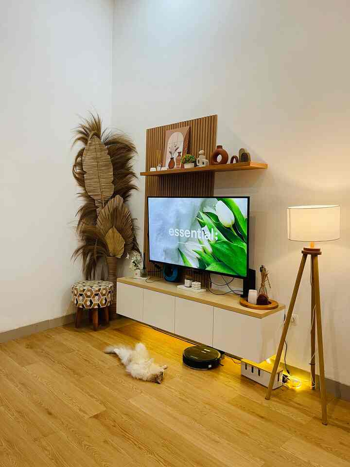 Natural wood-toned living room with white walls featuring TV, patterned stool, and floor lamp in a cozy setting