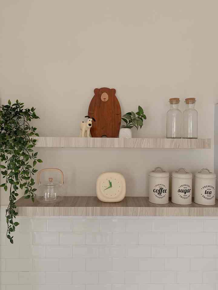 Natural wood tone and white tiled kitchen shelves featuring a bear-shaped cutting board and green plants in a tidy arrangement