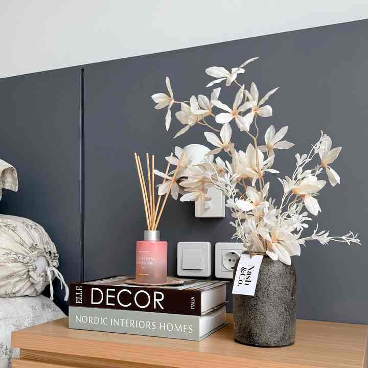 Charcoal wall and wood-tone bedside table in a stylish bedroom corner featuring diffuser and a vase with white flowers