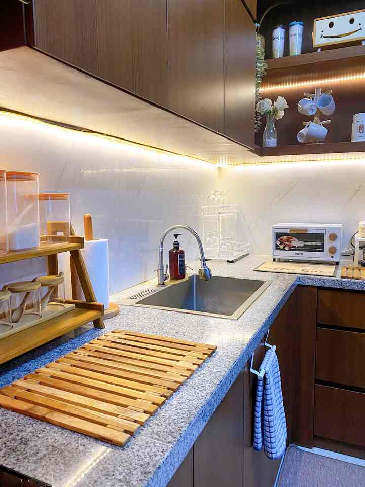 A cozy kitchen space featuring white walls and wood tone cabinets, kitchen sink, and a mini oven