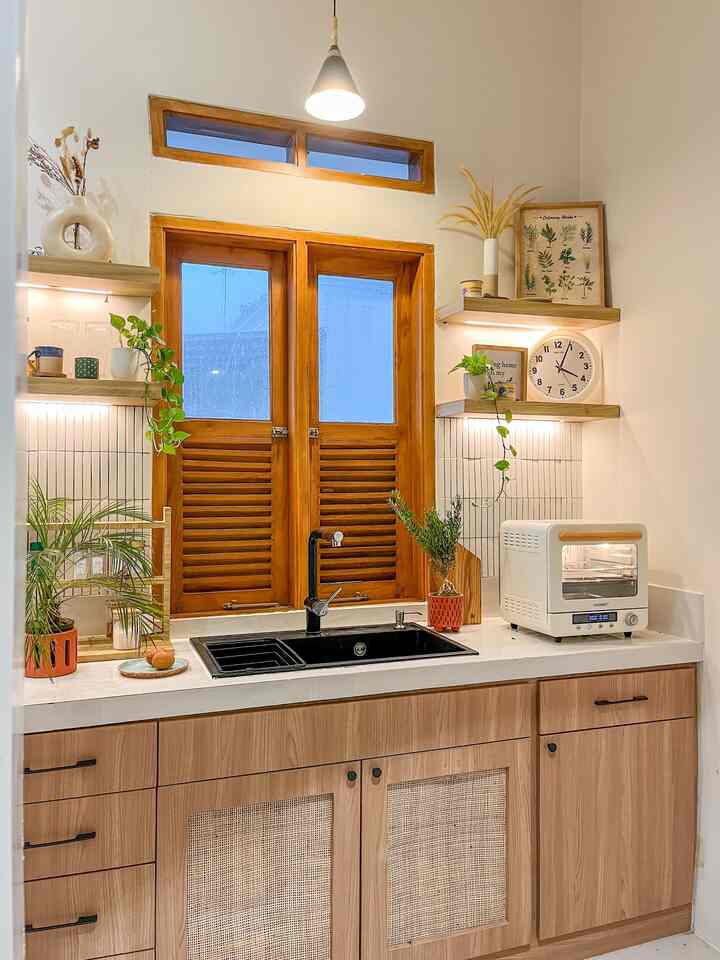 A white-walled kitchen featuring wood tone cabinetry, decorated with plants and kitchen utensils, creating a cozy and clean atmosphere