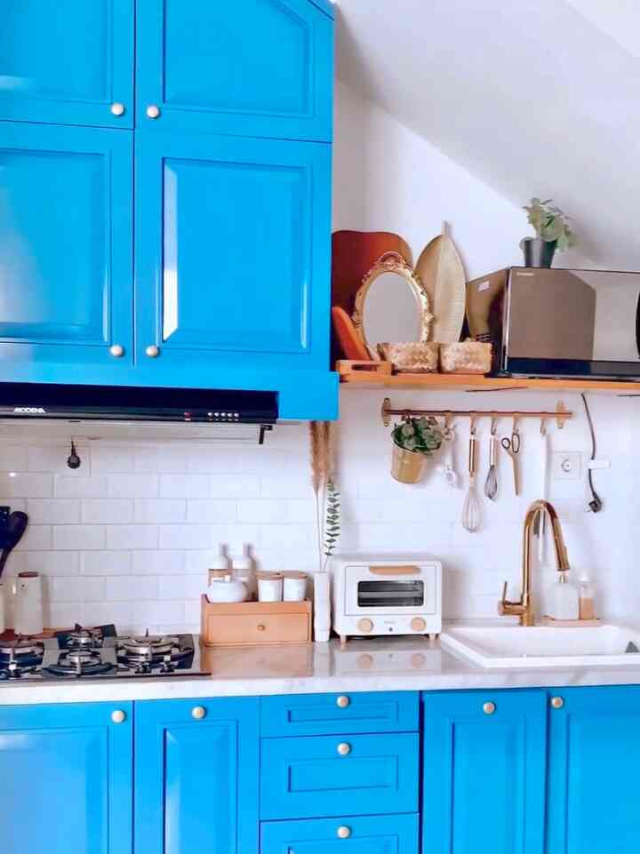 Compact kitchen with bright blue cabinets, gold faucet, and white tiled backsplash creating a clean and modern atmosphere