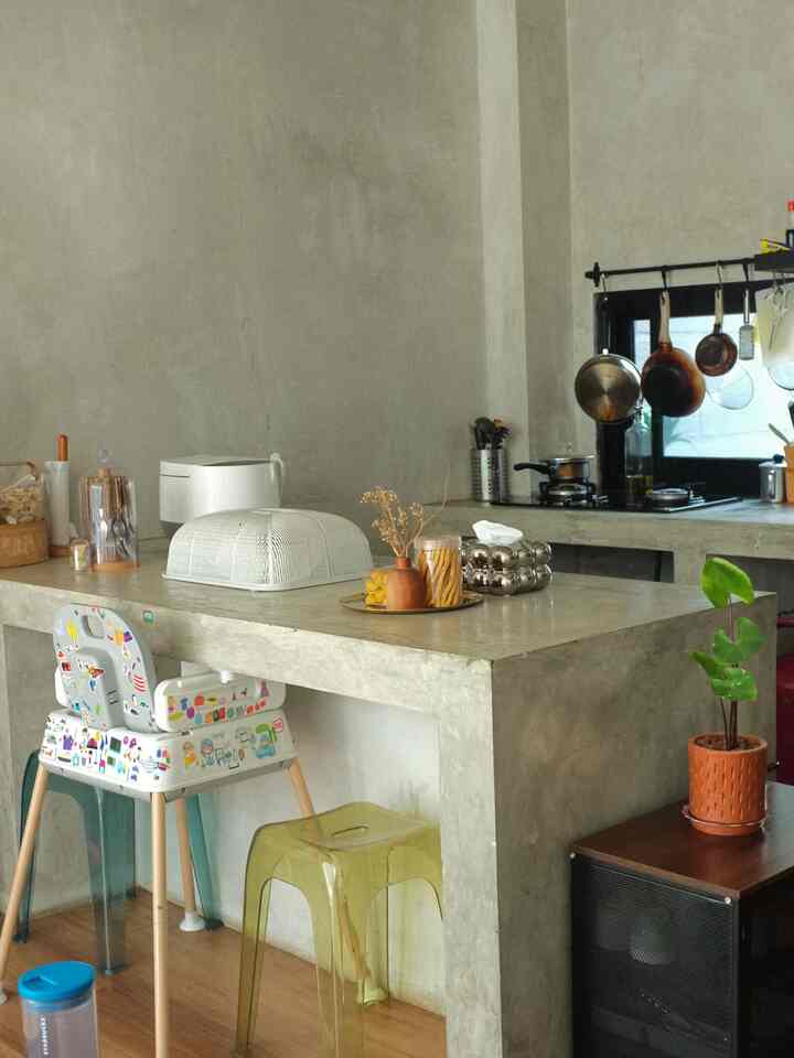 Gray-toned concrete kitchen and dining area featuring transparent stools and a child high chair with natural cozy atmosphere