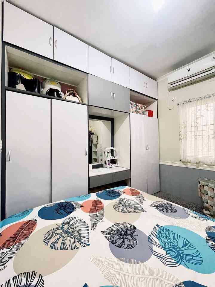 Small bedroom in white and natural tones featuring large wardrobes and patterned bedspread, creating a cozy space