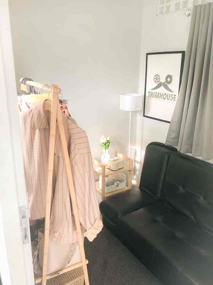 A small bedroom with white walls and wood-toned clothes rack featuring a black sofa bed and gray curtains creating a simple interior