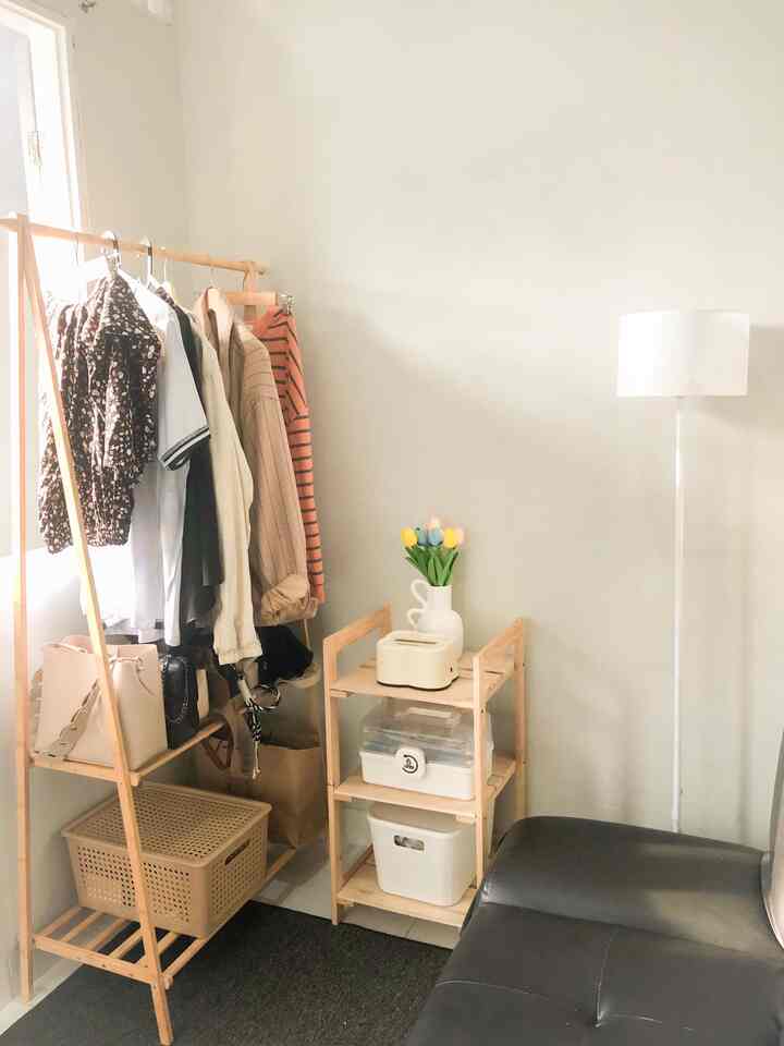 A small single household room with natural wood tones and white accents, featuring a clothing rack, shelving unit, and black sofa in a tidy setting