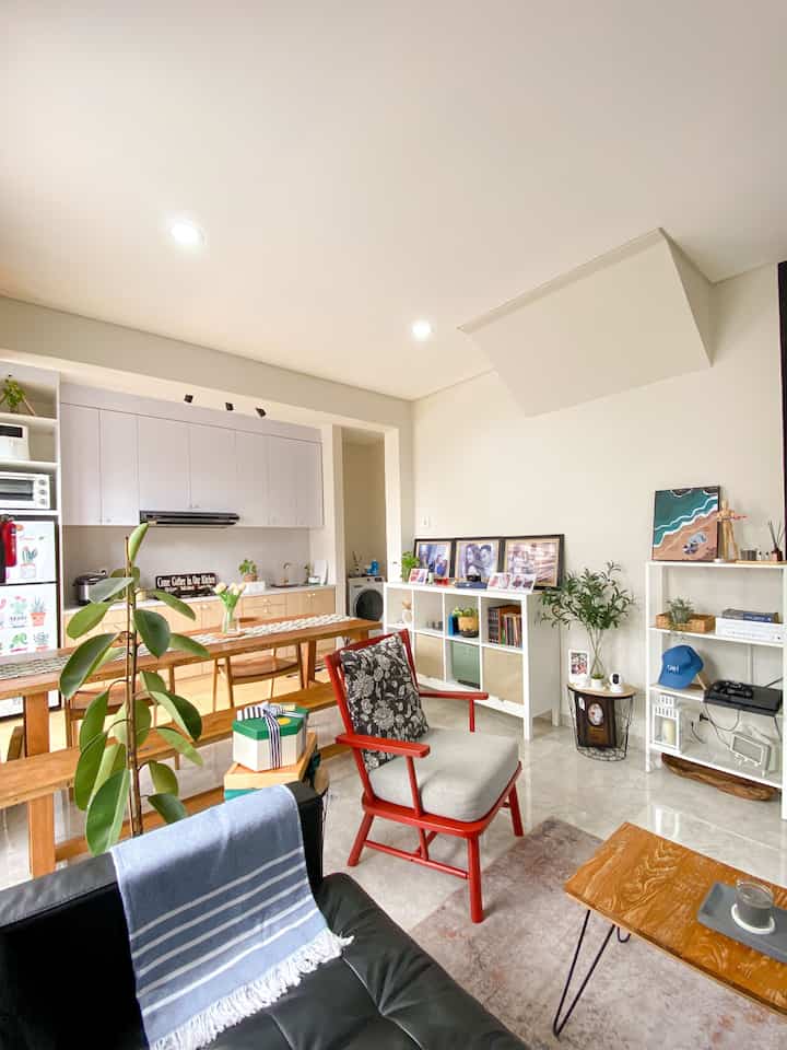 White and wood-toned open plan living room and kitchen featuring simple furnishings and storage units in a natural setting