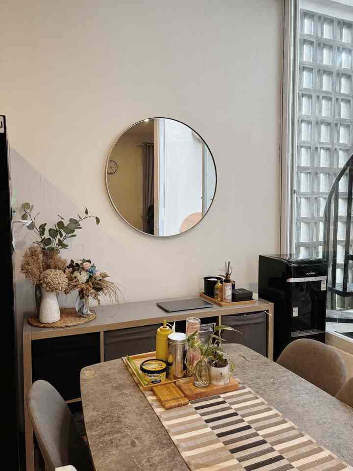 Beige natural toned dining room featuring a round mirror, table runner, and storage cabinet with a cozy atmosphere