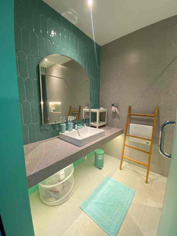 A stylish bathroom with green tiles and gray tones, featuring an arched mirror and wooden towel rack in a clean setting