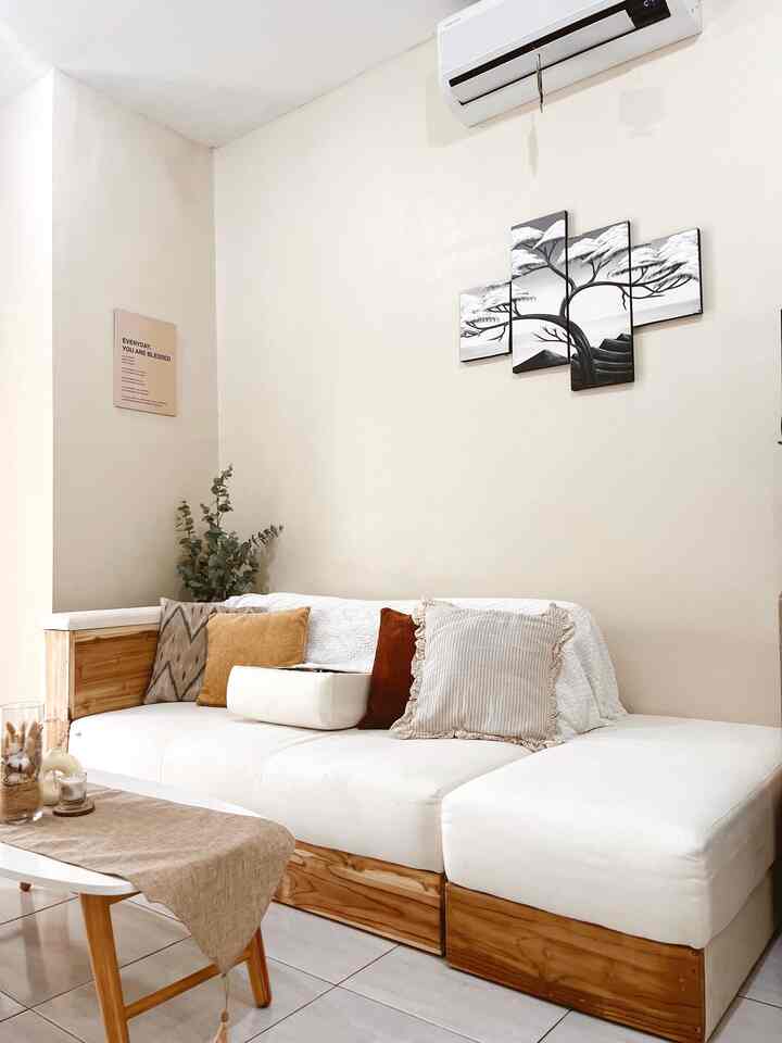 A cozy living room with beige walls and a white cushioned sofa, featuring wooden sofa base and a small table adding natural tones
