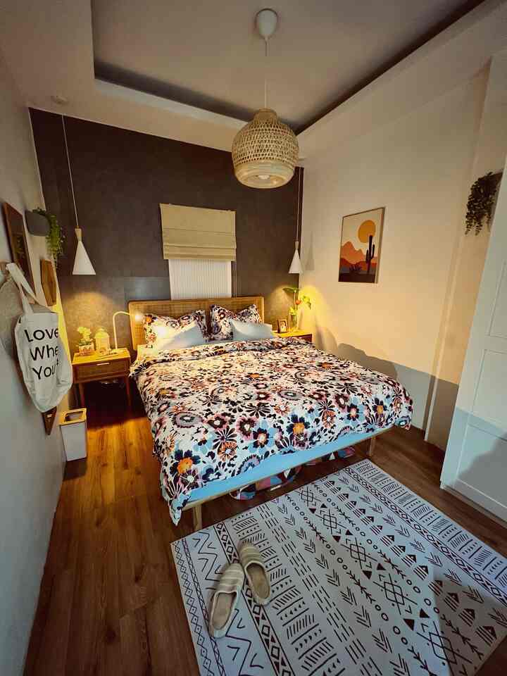 Cozy bedroom with light brown wood floor and rattan pendant light, floral bedding and nightstands arranged