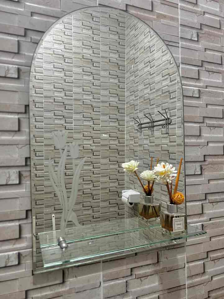 Gray brick-patterned tiled bathroom wall with an arched mirror, glass shelf, and reed diffuser creating a clean look