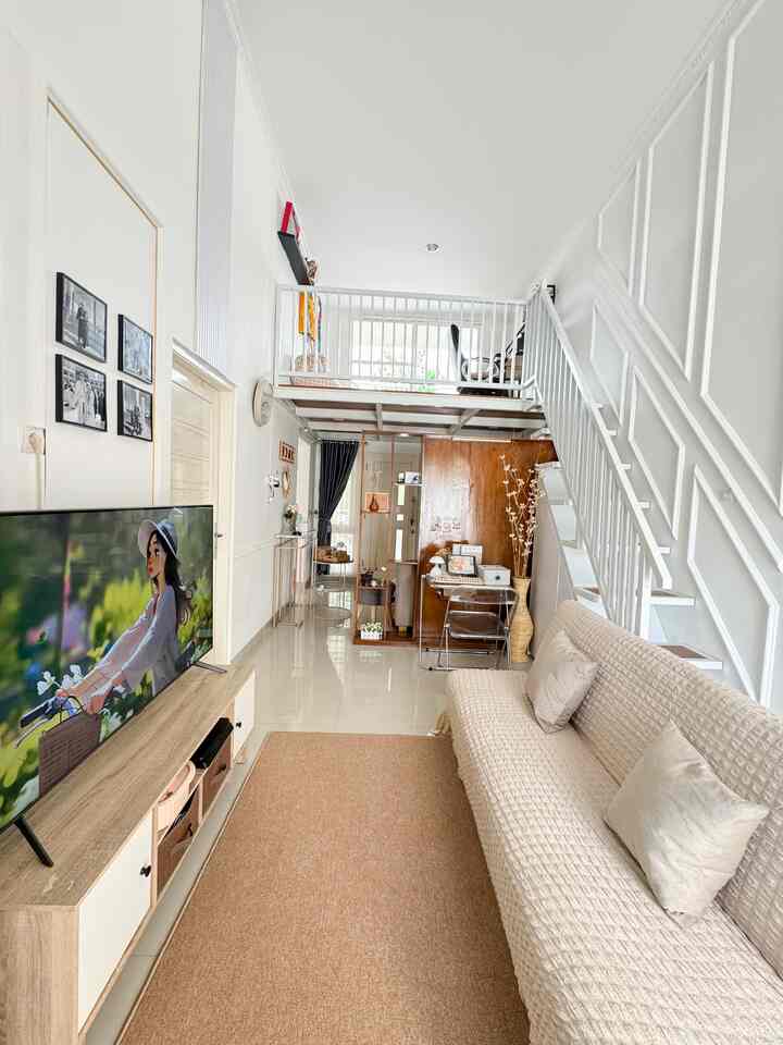 White and beige toned narrow living space featuring a loft mezzanine, stairs, beige sofa, and desk for compact functionality