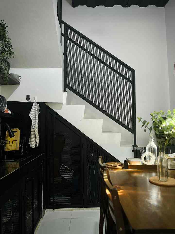 Industrial style kitchen and dining area with white walls and stairs, black perforated metal doors under stairs