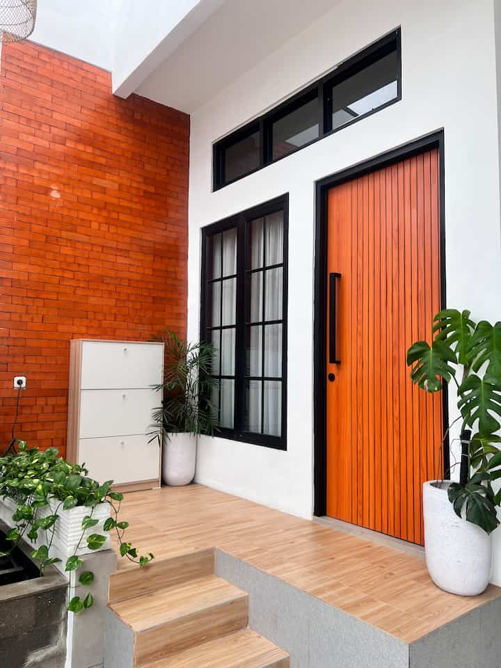 Modern entrance terrace featuring warm wood tones and terracotta wall, with black-framed windows and large plant pots arranged neatly