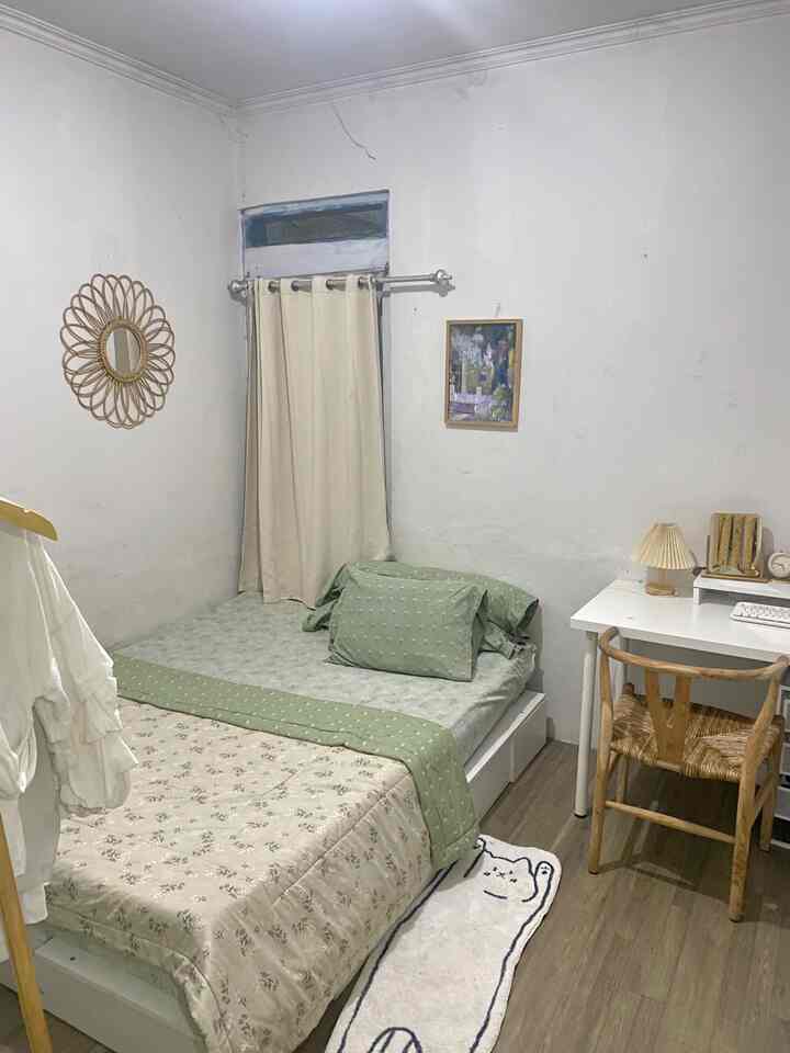 Natural beige and green toned bedroom featuring bed, rattan mirror, wooden chair, and simple desk creating a cozy atmosphere